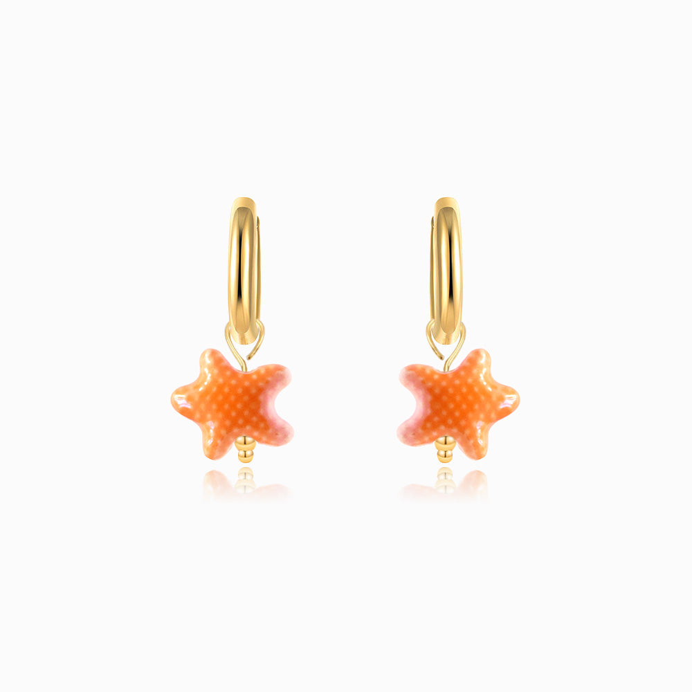 Gold hoop earrings with orange ceramic starfish on a white background