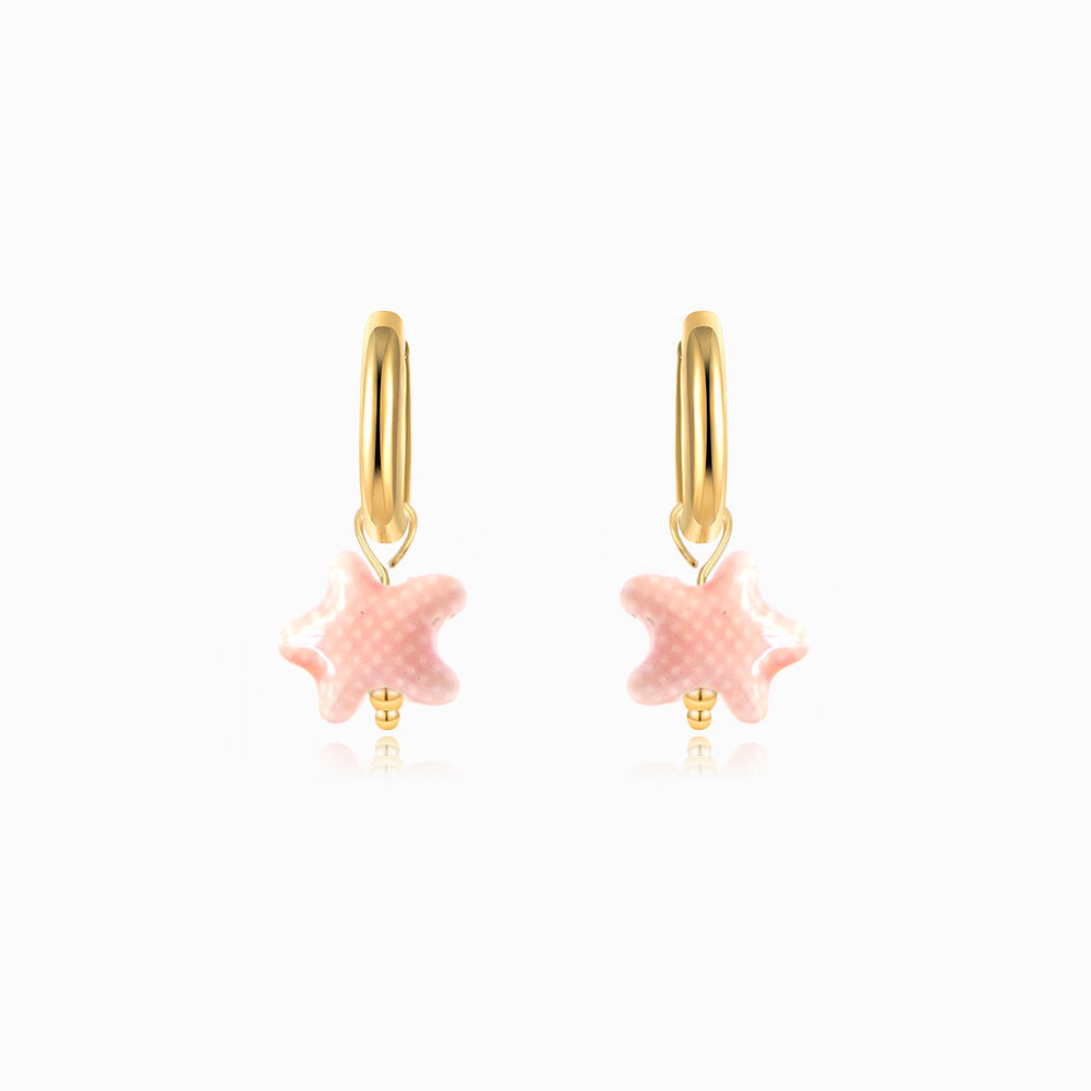 Gold hoop earrings with pink starfish charms on a white background