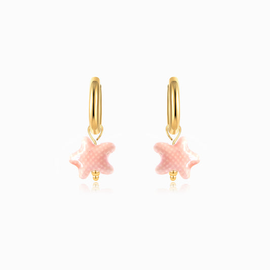Gold hoop earrings with pink starfish charms on a white background