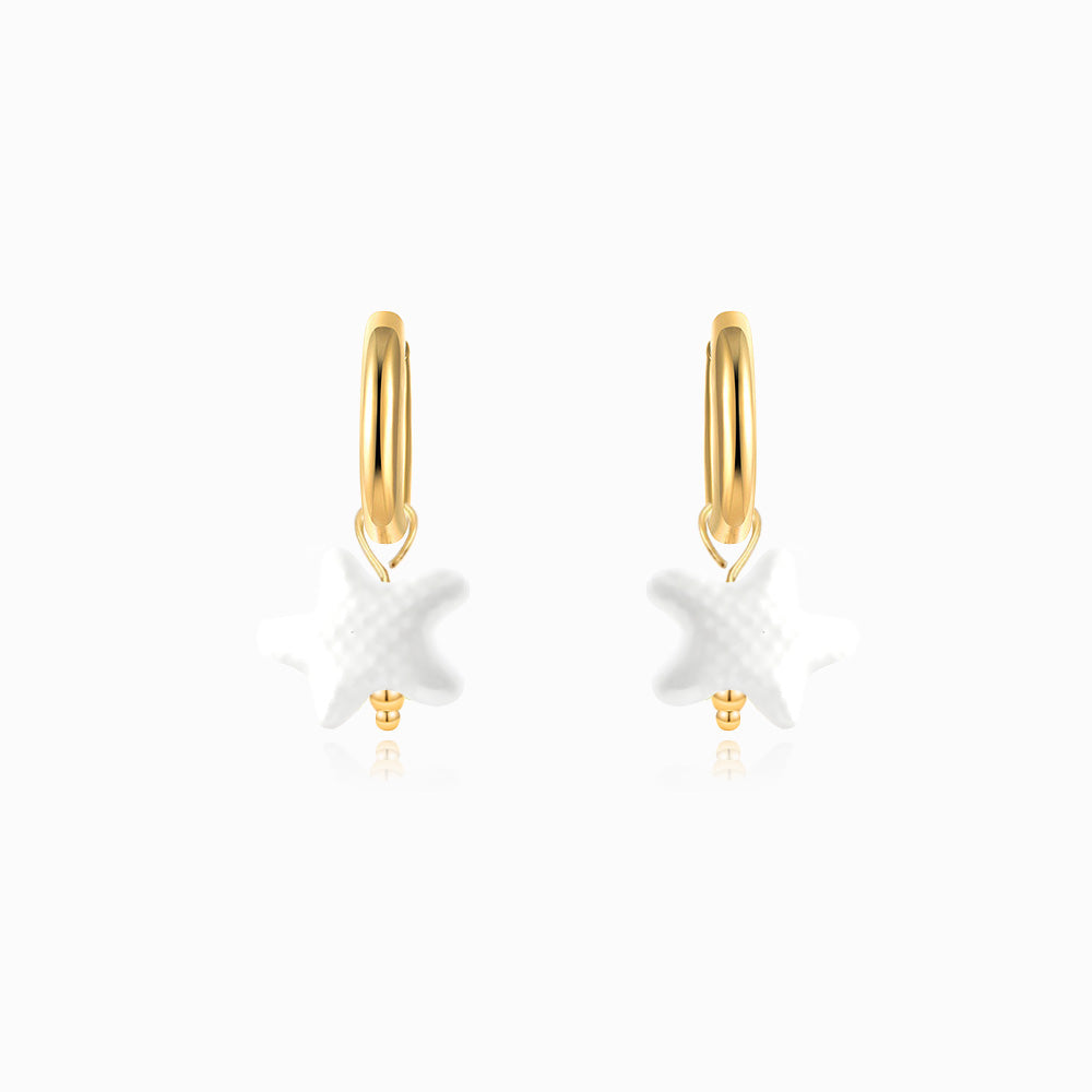Gold hoop earrings with white starfish charms on a white background